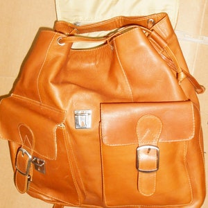 Pu&ograve; includere: Uno zaino in pelle marrone con due grandi tasche anteriori e una tasca pi&ugrave; piccola con chiusura a fibbia. Lo zaino ha una chiusura a coulisse e una patta con una fibbia.
