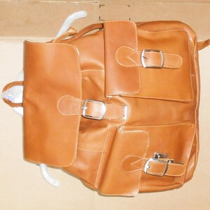 Pu&ograve; includere: Uno zaino in pelle marrone con pi&ugrave; tasche e fibbie. Lo zaino ha una patta con chiusura a fibbia e due tasche pi&ugrave; piccole sul davanti.