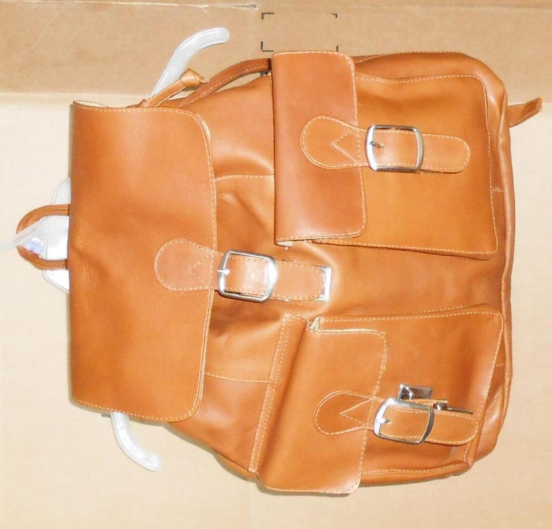 Pu&ograve; includere: Uno zaino in pelle marrone con pi&ugrave; tasche e fibbie. Lo zaino ha una patta con chiusura a fibbia e due tasche pi&ugrave; piccole sul davanti.