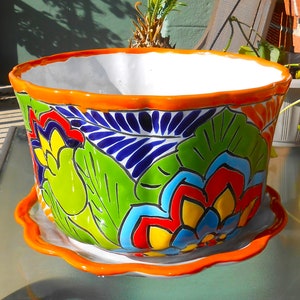 May include: A colorful ceramic planter with a scalloped rim and a matching saucer. The planter features a floral design with blue, green, red, yellow, and white flowers.