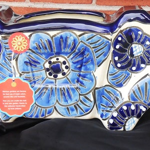 May include: A white ceramic planter with blue and white floral designs. The planter has three sections, each with a separate opening for planting. The planter is decorated with blue and white floral designs.