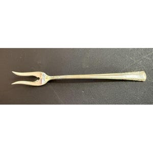 May include: A silver-plated serving fork with a decorative handle. The fork has two prongs and a long, slender handle.