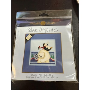 May include: A cross-stitch kit labelled "Polar Opposites" showing a polar bear and a penguin. The design size is 12.7 cm x 12.07 cm. The kit includes a blue border and a white background with the text "Polar Play".
