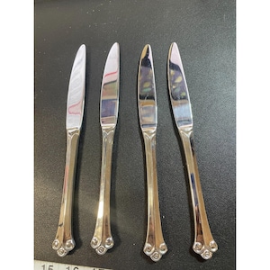 Pode incluir: Quatro facas de jantar de prata com cabos ornamentados. Os cabos têm um design de redemoinho na extremidade.