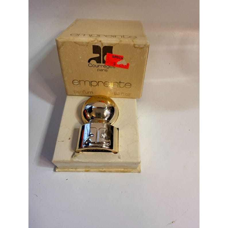 May include: A vintage Courr&egrave;ges Empreinte perfume bottle with a gold-colored spherical top and a silver-colored base. The perfume bottle is displayed in its original box, which has the brand name and logo printed on it. The box has a red sticker.