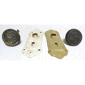 May include: Three antique door knobs with keyhole plates. Two plates are painted white and gold, and one knob is brass with a floral design.