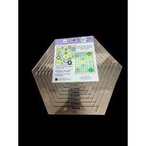 May include: A clear acrylic hexagon ruler labeled You Hexie Thing with black printed markings for finished sizes from 2 inches to 5 inches. The tool includes a paper insert showing quilt patterns and instructions for cutting fabric strips.
