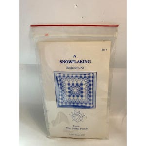 Op de afbeelding: Een "Snowflaking Beginner's Kit" in een doorzichtige plastic zak. De kit bevat een wit papier met tekst en een afbeelding van een blauw-wit sneeuwvlokontwerp. De tekst luidt "A SNOWFLAKING Beginner's Kit" en "from The Berry Patch".