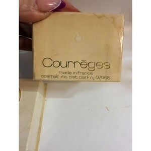 May include: A rectangular, beige box with the brand name "Courr&egrave;ges" in a gold font. The text "made in france" and the address "cosmair inc. dist. clark nj 07066" are also visible.
