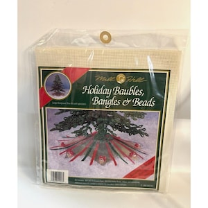 May include: A Mill Hill Holiday Baubles, Bangles & Beads craft kit featuring a green evergreen tree with red and green ribbon and red and white ornaments. The kit includes perforated paper, printed fabric, beads, ribbon and instructions.