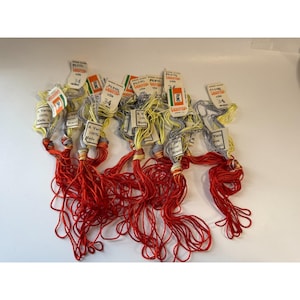 Op de afbeelding: Een verzameling borduurgaren in verschillende kleuren, waaronder rood, geel en grijs. Elke streng heeft een papieren label met het nummer 34 en de merknaam "Varicor". Het garen is gemaakt van rayon en is 100% gemaakt in Brazilië.