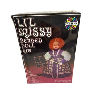May include: A box for a beaded doll kit featuring a teacher doll with a purple dress and a chalkboard. The box is black with a red and white design and the text "Lil' Missy Beaded Doll Kit" and "Holiday".