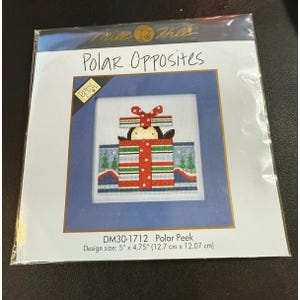 Puede incluir: Un kit de punto de cruz titulado "Polar Opposites" con un diseño de un pingüino saliendo de una caja de regalo. El tamaño del diseño es de 12,7 cm x 12,07 cm. El kit incluye el texto "Polar Peek" y la marca "Mill Hill".