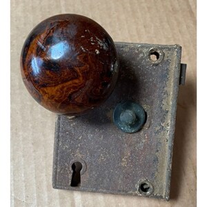 May include: A vintage door knob with a brown and black marbled ceramic sphere and a metal plate with a keyhole.