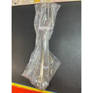 May include: A silver cake server with a decorative swirl design on the handle. The server is wrapped in clear plastic.