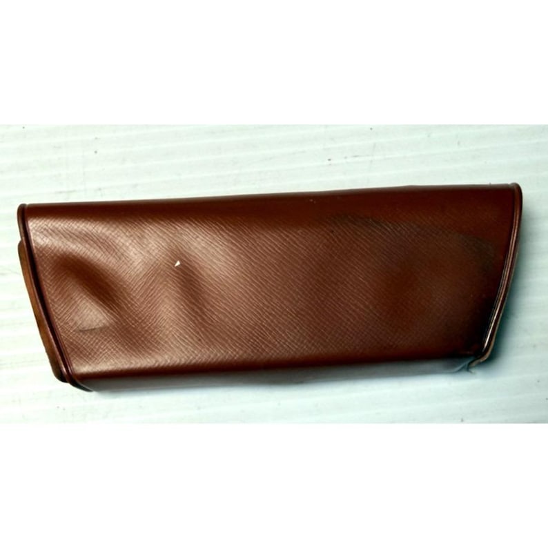 May include: A rectangular, brown, hard-shell glasses case with a textured, cross-hatched surface pattern. The case features a hinged lid design with a smooth, slightly curved front profile and tapered sides, providing a secure enclosure.