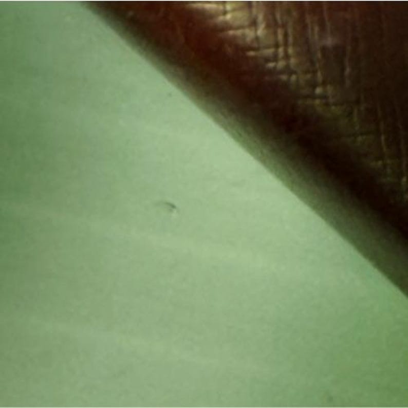 May include: A split composition featuring a smooth, light mint green surface on the bottom left and a dark brown, textured material with a cross-hatched pattern on the top right, meeting along a diagonal line that divides the two distinct sections.