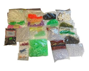 May include: A variety of colorful plastic beads in bags, including clear, green, black, white, and red beads. The bags are labeled with the brand "Craft Destiner" and "The Reader".