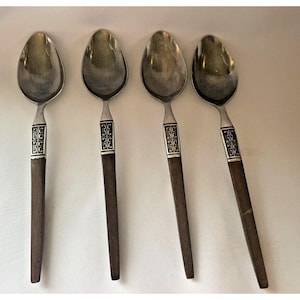 May include: Four silver spoons with brown wooden handles. The handles have a decorative pattern of black squares with a stylized floral design.