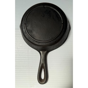 May include: A well-worn, cast iron skillet with a long handle and a circular cooking surface. The skillet is dark gray with a smooth interior and a raised rim. The handle has a hole for hanging. The skillet is designed for stovetop or oven use.