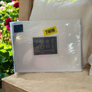 May include: A white twin-sized sheet set in a plastic package. The package has a label that says "Pure Home by Indigo" and "Twin".