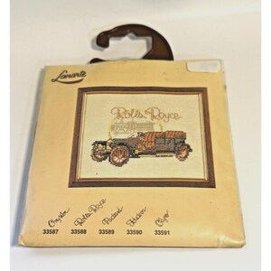 May include: A vintage cross-stitch pattern featuring a Rolls Royce car with the text "Rolls Royce" above it. The pattern is on a beige background with a brown frame. The pattern is part of a set of cross-stitch patterns, with the numbers 33587, 33588, 33589, 33590, and 33591 listed below the pattern.