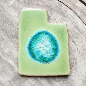 May include: A green ceramic tile shaped like the state of Utah with a blue and green circle in the center.