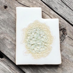 May include: A white ceramic tile shaped like the state of Utah with a green and yellow design in the center.