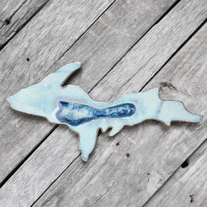 May include: A light blue ceramic wall hanging in the shape of the Upper Peninsula of Michigan. The hanging has a blue glaze with a darker blue center.