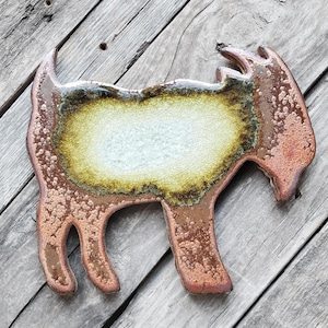 May include: A ceramic goat figurine with a brown, green, and white glaze. The figurine is in a standing position with its head turned to the side.