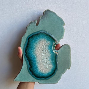 May include: A ceramic Michigan state outline with a teal and white glaze. The outline is raised and the glaze is textured.