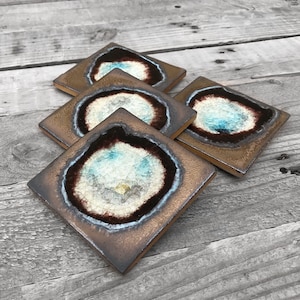 May include: Set of four square ceramic coasters with a geode design. Each coaster features a brown background with a white and blue geode pattern in the center.