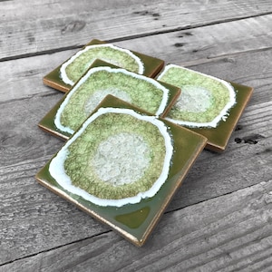 May include: Set of four green and white ceramic coasters with a geode design. The coasters have a white rim and a green center with a white crystal-like pattern.