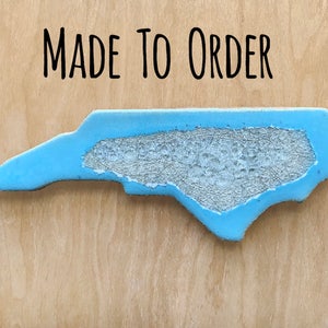 May include: A blue painted wooden cutout of the state of North Carolina, with the words "MADE TO ORDER" above it.