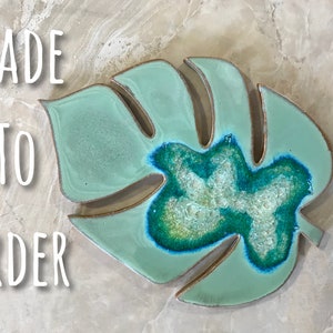 May include: A light green ceramic monstera leaf with a blue and green agate inlay. The leaf is made to order. "MADE TO ORDER" is written in white text on a light brown background.