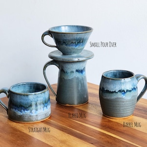 May include: A collection of handmade ceramic mugs and a small pour-over coffee maker. The mugs include a straight mug, flared mug, and barrel mug, all with a blue and gray glaze. The text on the image reads "Small Pour Over", "Flared Mug", "Straight Mug", and "Barrel Mug".