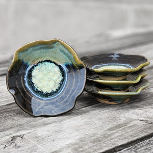 May include: Four small, handmade ceramic dishes with a blue, green, and black glaze. The dishes have a scalloped edge and a raised center.