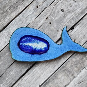 May include: A blue ceramic whale-shaped dish with a blue and white agate-like design in the center. The dish is on a weathered wooden surface.