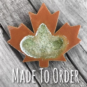 May include: A rusty brown metal maple leaf with a green and white glass center. The leaf is on a wooden surface. MADE TO ORDER.