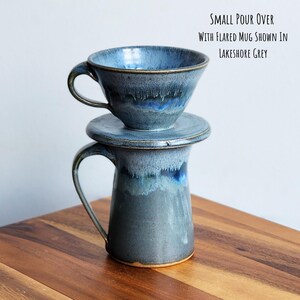 May include: A ceramic pour-over coffee set in a Lakeshore Grey glaze. The set includes a flared mug, a pour-over cone, and a lid. The mug has a handle. The text on the image reads: "SMALL POUR OVER WITH FLARED MUG SHOWN IN LAKESHORE GREY."