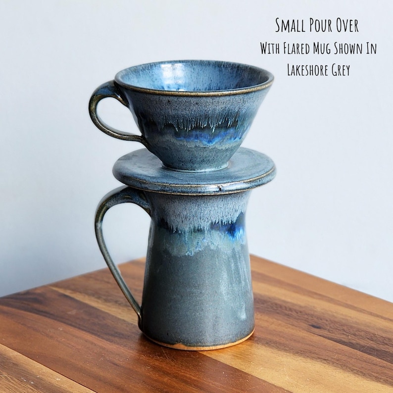 May include: A ceramic pour-over coffee set in a Lakeshore Grey glaze. The set includes a flared mug, a pour-over cone, and a lid. The mug has a handle. The text on the image reads: "SMALL POUR OVER WITH FLARED MUG SHOWN IN LAKESHORE GREY."