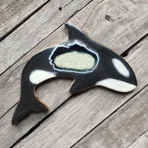 May include: A ceramic wall hanging in the shape of an orca, painted black and white with a blue and green glaze detail.