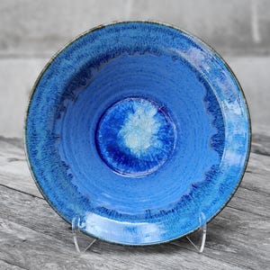 May include: A blue ceramic bowl with a white and blue glaze. The bowl has a deep, round shape and a wide rim.
