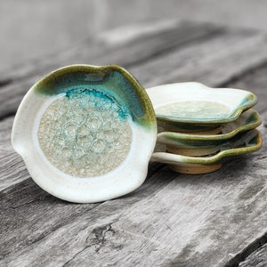 May include: Set of four small, white ceramic dishes with a green and blue glaze. The dishes have a wavy edge and a textured center.