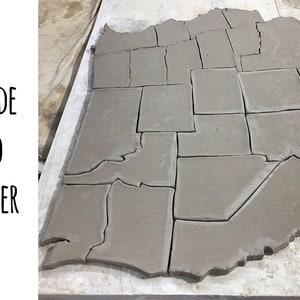 May include: A gray clay model of the United States, divided into individual states. The clay is still wet and has a rough texture.