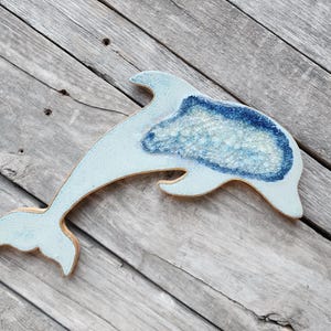 May include: A light blue ceramic dolphin sculpture with a blue and white mosaic design. The dolphin is leaping out of the water.