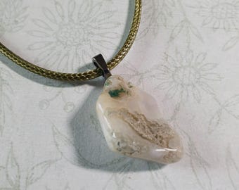 Puede incluir: Un colgante de ágata blanco y verde en un collar de cordón verde. El colgante tiene una forma libre con una anilla de plata.