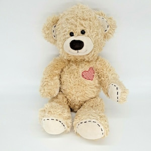 May include: A plush teddy bear with light brown fur, black button eyes, and a black nose. The bear has a red and white heart-shaped patch on its chest and stitched details on its paws and ears. A cuddly toy.