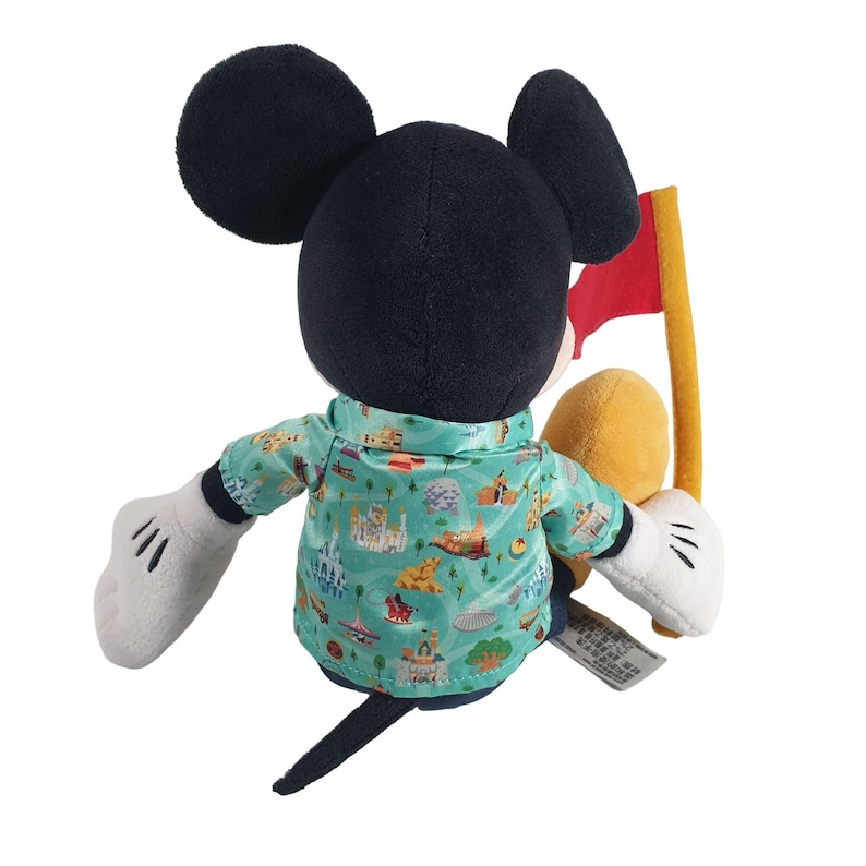 May include: A plush Mickey Mouse wearing a green and blue Hawaiian shirt with a pattern of Disney park attractions. Mickey is holding a yellow plush figure and a red flag.