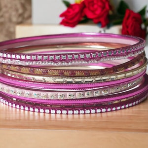 May include: A set of pink and silver bangles with glitter accents. The bangles are stacked on top of each other and have a shiny finish.